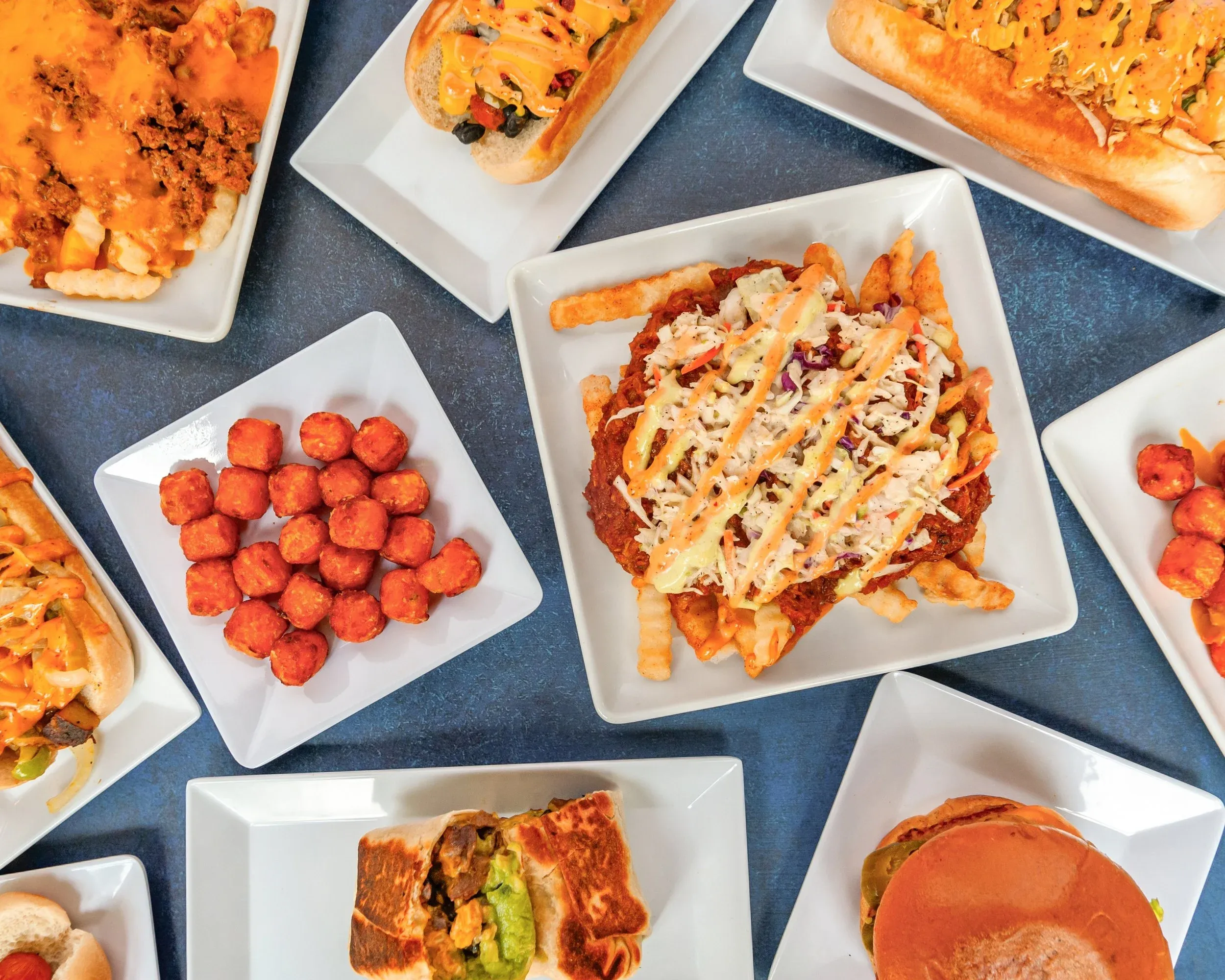 Overhead spread of Mike's vegan comfort food: chili fries, burgers, sweet potato tots and more